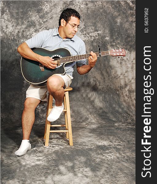An man in shorts sitting on a chair with an green guitar for a black 
and white background. An man in shorts sitting on a chair with an green guitar for a black 
and white background.