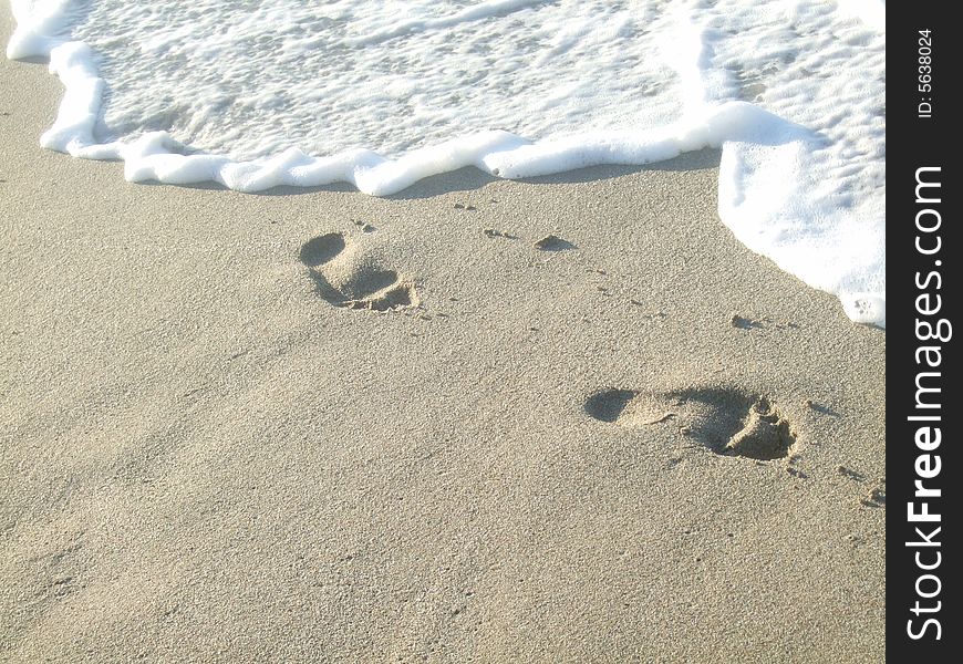 The footprints on the sea sand and wave (background)