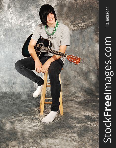 An boy in black jeans sitting on a chair with an green guitar for a black 
and white background and smiling in the camera. An boy in black jeans sitting on a chair with an green guitar for a black 
and white background and smiling in the camera.