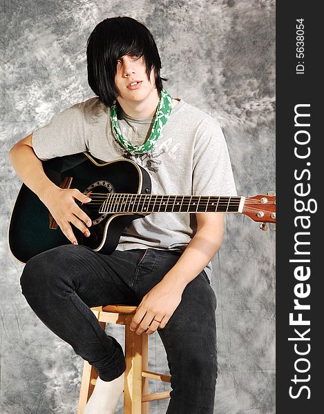 An boy in black jeans sitting on a chair with an green guitar for a black 
and white background. An boy in black jeans sitting on a chair with an green guitar for a black 
and white background.