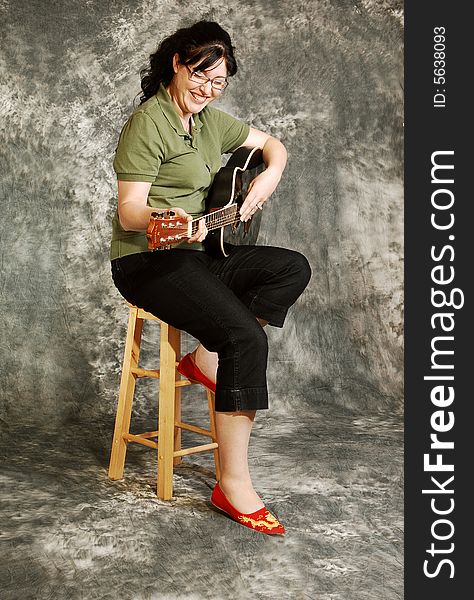 An woman in black pants sitting on a chair with an green guitar for a black and white background and smiling in the camera. An woman in black pants sitting on a chair with an green guitar for a black and white background and smiling in the camera.