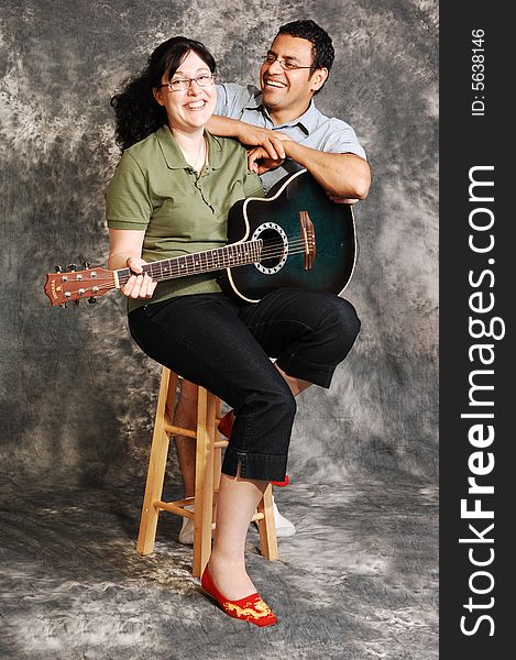 An woman in black pants sitting on a chair with an green guitar for a black 
and white background and smiling in the camera, with her husband. An woman in black pants sitting on a chair with an green guitar for a black 
and white background and smiling in the camera, with her husband.