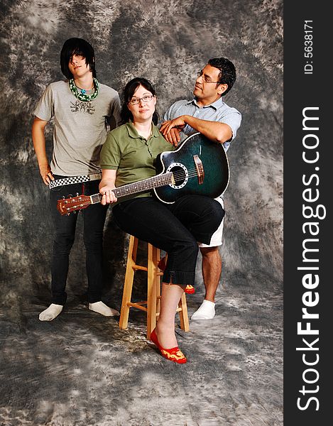 An woman in black pants sitting on a chair with an green guitar for a black 
and white background and smiling in the camera, with her husband and son. An woman in black pants sitting on a chair with an green guitar for a black 
and white background and smiling in the camera, with her husband and son.