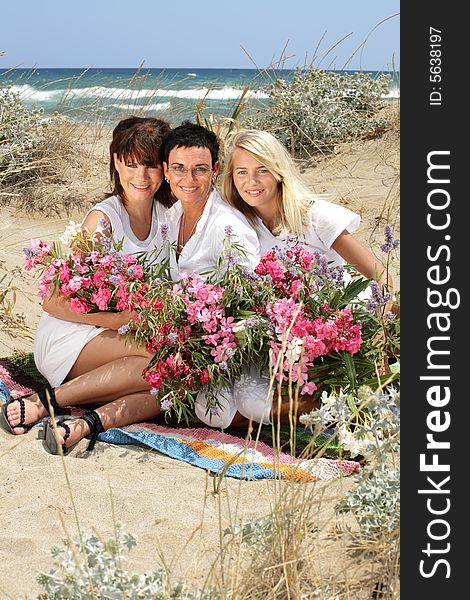 Beautiful mother and daughters holding flowers sitting on the beach. Beautiful mother and daughters holding flowers sitting on the beach