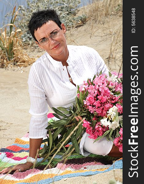 Beautiful woman holding flowers sitting on the beach