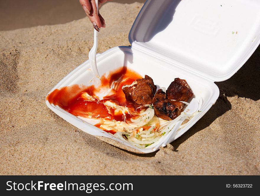 Female hand with a fork is taking a slice kebab from container closeup