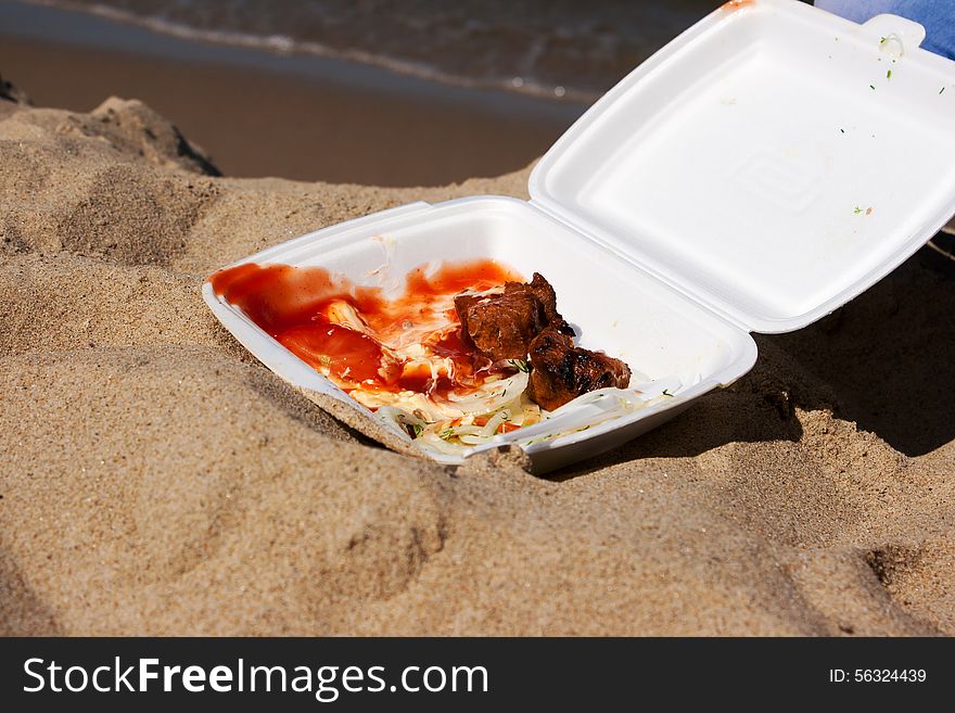 Two slices shashlik with onions and sauce in a container on the sand outside closeup