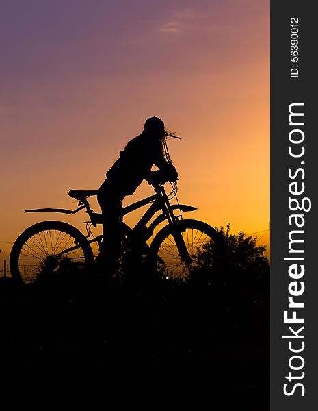а Silhouette of a gerl with a bicycle against the sky at sunset,