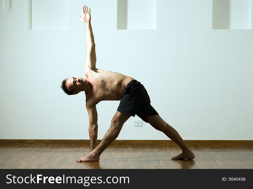 Man in a yoga pose with one arm extended up and the other down and his legs apart. Horizontally framed photograph. Man in a yoga pose with one arm extended up and the other down and his legs apart. Horizontally framed photograph