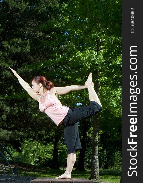 Woman smiles as she does a yoga pose in the park. Vertically framed photograph. Woman smiles as she does a yoga pose in the park. Vertically framed photograph.