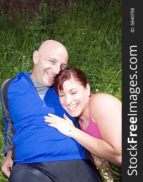 Happy couple sit on the grass in the park. She is leaning on his shoulder and they are laughing. Vertically framed photograph. Happy couple sit on the grass in the park. She is leaning on his shoulder and they are laughing. Vertically framed photograph