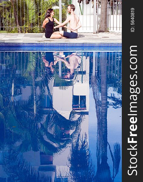 A couple, sit down by the pool, crossing arms, stretching, smiling at each other - vertically framed. A couple, sit down by the pool, crossing arms, stretching, smiling at each other - vertically framed