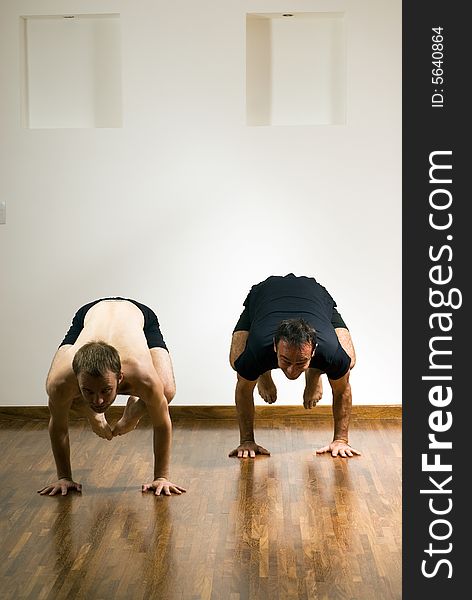 Two men practicing yoga in a studio. They are in a crouch position with their feet off the floor. Vertically framed photograph. Two men practicing yoga in a studio. They are in a crouch position with their feet off the floor. Vertically framed photograph