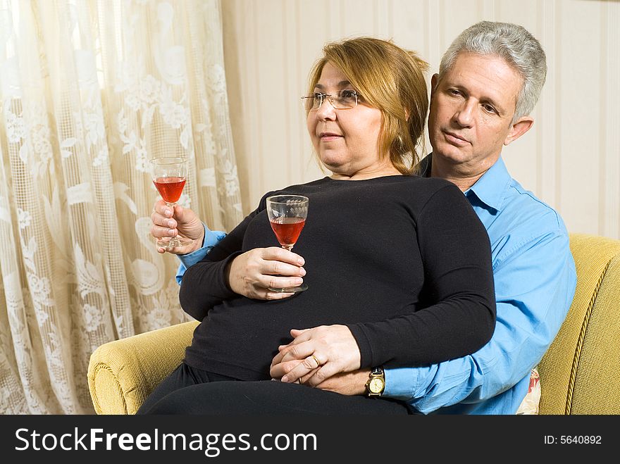 A couple relaxing with wine glasses. The female figure is seated on the male's lap. She is smiling. Horizontally framed shot. A couple relaxing with wine glasses. The female figure is seated on the male's lap. She is smiling. Horizontally framed shot.