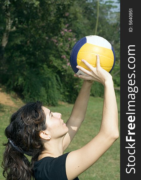 A woman is standing in a park.  She is looking away from the camera.  She is playing volleyball.  Vertically framed photo. A woman is standing in a park.  She is looking away from the camera.  She is playing volleyball.  Vertically framed photo.