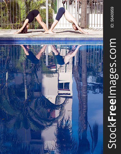 A couple, in a v-shape, stretch by the poolside - vertically framed. A couple, in a v-shape, stretch by the poolside - vertically framed