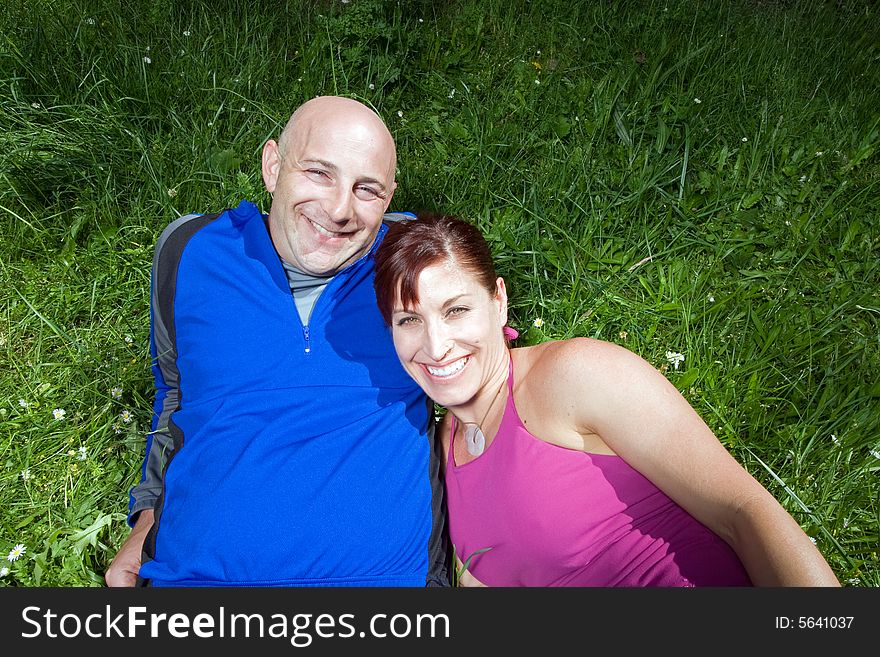 Happy couple sit on the grass in the park. She is leaning on his shoulder. Horizontally framed photograph. Happy couple sit on the grass in the park. She is leaning on his shoulder. Horizontally framed photograph