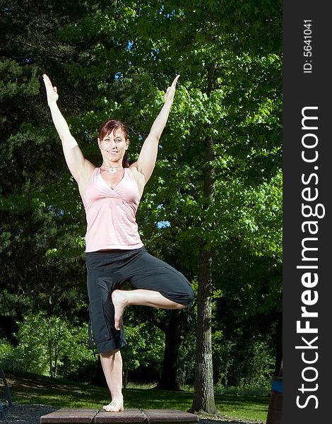 Woman smiles as she does a yoga pose in the park. Vertically framed photograph. Woman smiles as she does a yoga pose in the park. Vertically framed photograph.