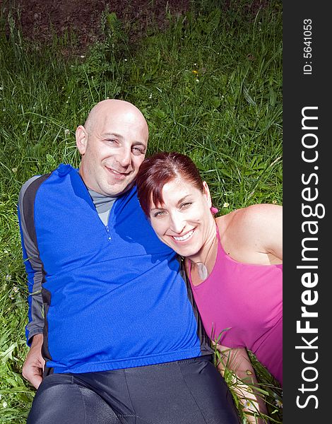 Happy couple sit on the grass in the park. She is leaning on his shoulder. Vertically framed photograph. Happy couple sit on the grass in the park. She is leaning on his shoulder. Vertically framed photograph