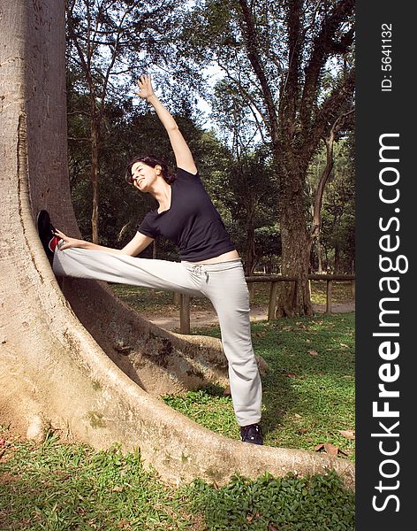 A smiling woman is standing next to a tree.  She is looking at the tree and stretching.  Vertically framed photo. A smiling woman is standing next to a tree.  She is looking at the tree and stretching.  Vertically framed photo.