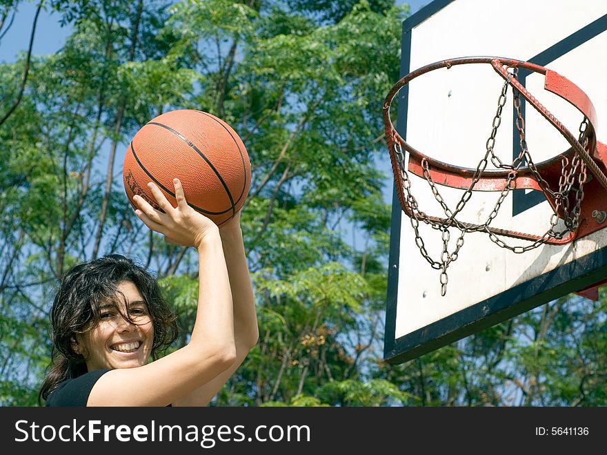 A smiling woman is playing basketball on a court at the park. The woman is looking at the camera and about to make a shot. Horizontally framed photo. A smiling woman is playing basketball on a court at the park. The woman is looking at the camera and about to make a shot. Horizontally framed photo.