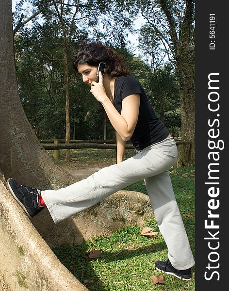 A young, attractive woman is standing next to a tree.  She is looking at her foot, and stretching her leg on the tree.  Vertically framed photo. A young, attractive woman is standing next to a tree.  She is looking at her foot, and stretching her leg on the tree.  Vertically framed photo.