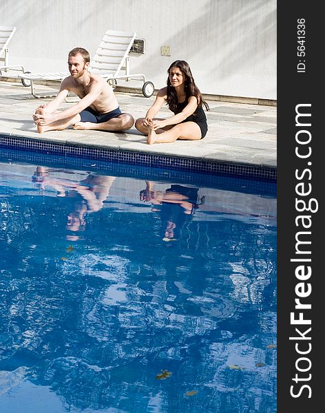 Couple stretching their legs by the poolside, smiling and concentrating - vertically framed. Couple stretching their legs by the poolside, smiling and concentrating - vertically framed