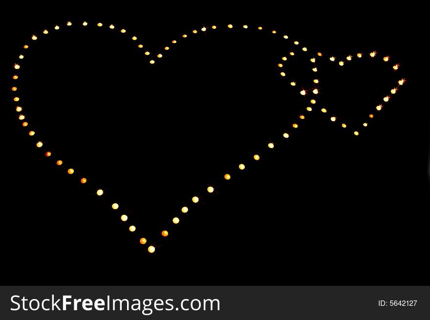 Shape of two crossed hearts made of small burning candles on black background. Shape of two crossed hearts made of small burning candles on black background