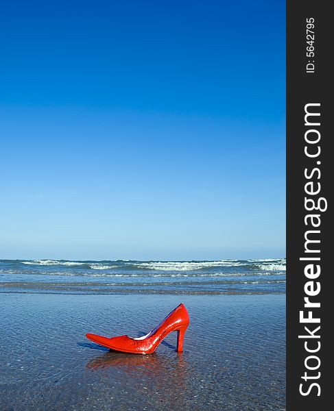 A red and pink stiletto shoe on a beach. A red and pink stiletto shoe on a beach