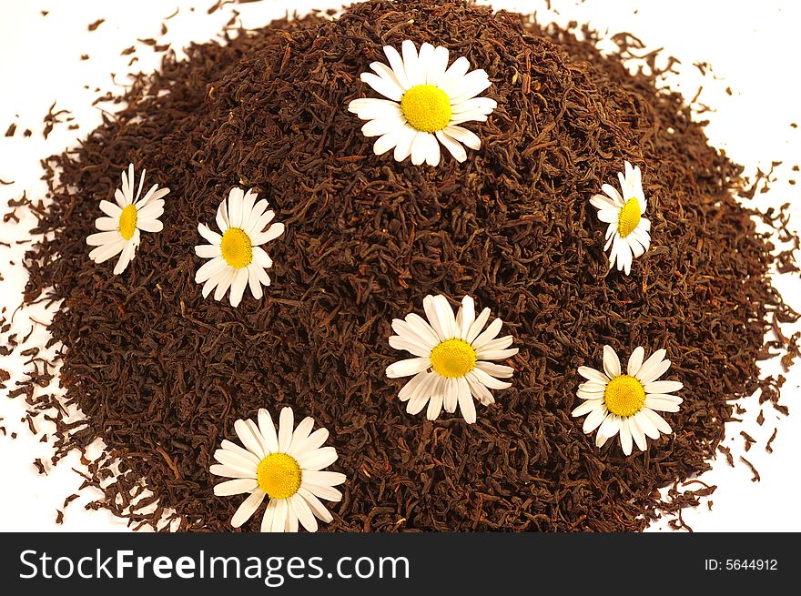 Heap of black tea and chamomile blossoms isolated on white