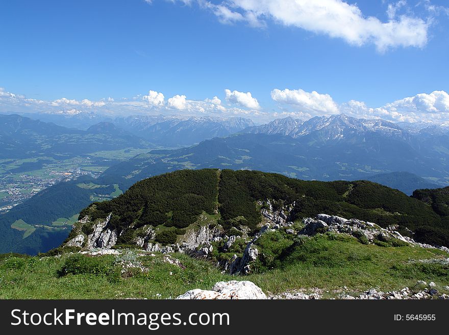 Clouds above the mountains Austrian  Alpes . Small Buildings and green fields at the distance .  Sight from the peak of Untersberg mountain .Not so far from Salzburg . Clouds above the mountains Austrian  Alpes . Small Buildings and green fields at the distance .  Sight from the peak of Untersberg mountain .Not so far from Salzburg .