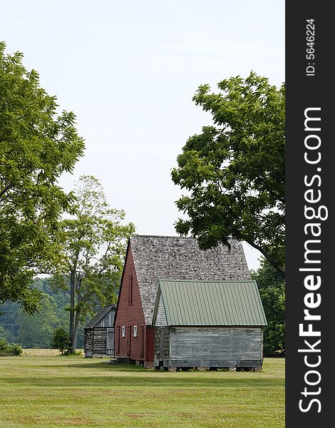 Old red wooden barn and two outbuildings in a wooded field. Old red wooden barn and two outbuildings in a wooded field.