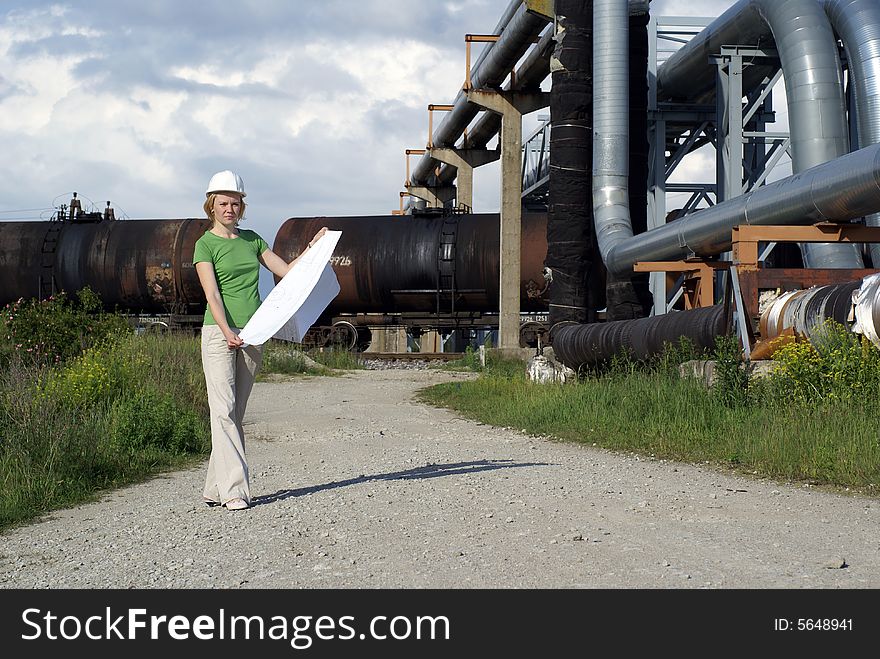 Woman engineer or architect with white safety hat, drawings and industrial pipelines on background. Woman engineer or architect with white safety hat, drawings and industrial pipelines on background