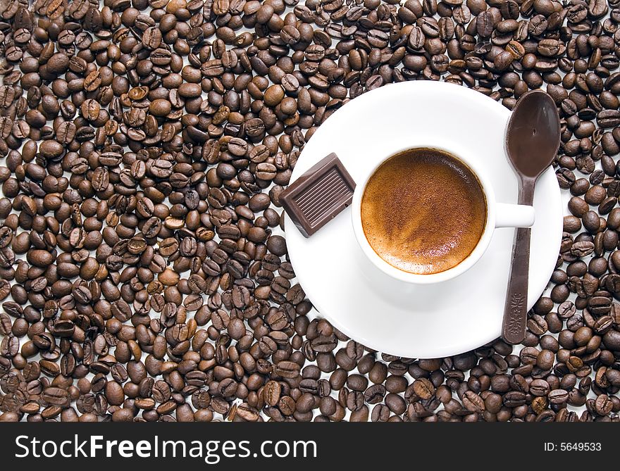 Overhead shot of a cup of coffee with a chocolate spoon and a piece of chocolate beside. Coffee beans background. Copy space. Overhead shot of a cup of coffee with a chocolate spoon and a piece of chocolate beside. Coffee beans background. Copy space.