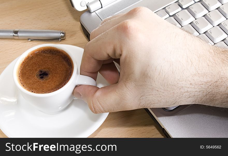 Close up of a hand taking a cup of coffee over a laptop. Close up of a hand taking a cup of coffee over a laptop.