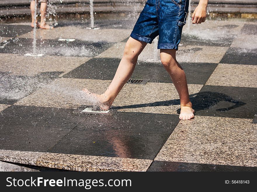 Feet of boy in blue jeans playing in the fountain on sunny summer day. Feet of boy in blue jeans playing in the fountain on sunny summer day