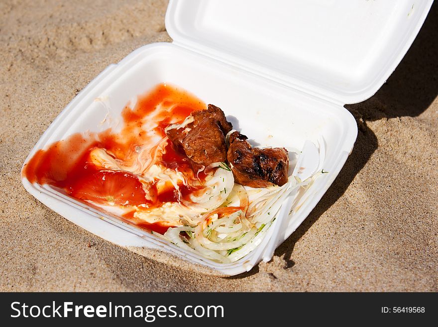 Two slices kebab with onions and sauce in a container on the sand outside closeup