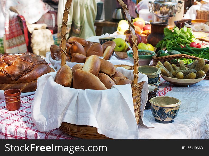 Cakes, Bread, Cucumbers, Radishes And Apples On A Table Outside