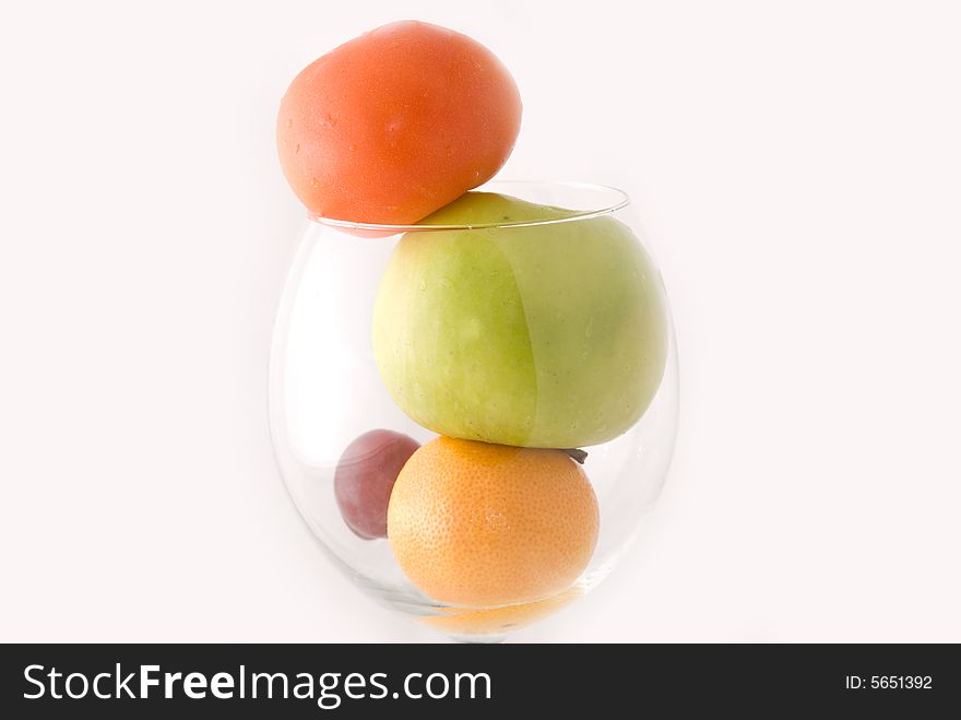 A cup of fresh fruits, including red tomato, green apple, orange, and red grape, on white background