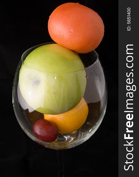 A cup of fresh fruits, including red tomato, green apple, orange, and red grape, on black background