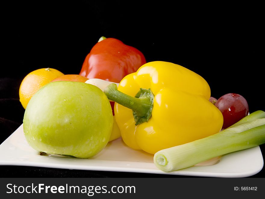 A plate of fresh fruits and vegetables on black background. A plate of fresh fruits and vegetables on black background.