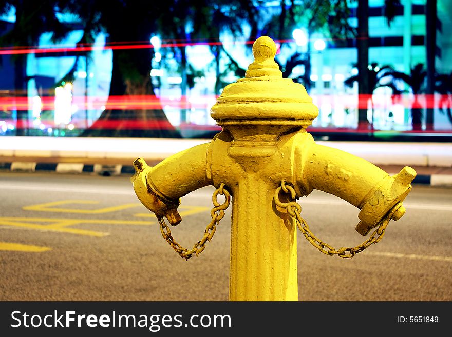 Long exposure of yellow fire hydrant beside road at night time.