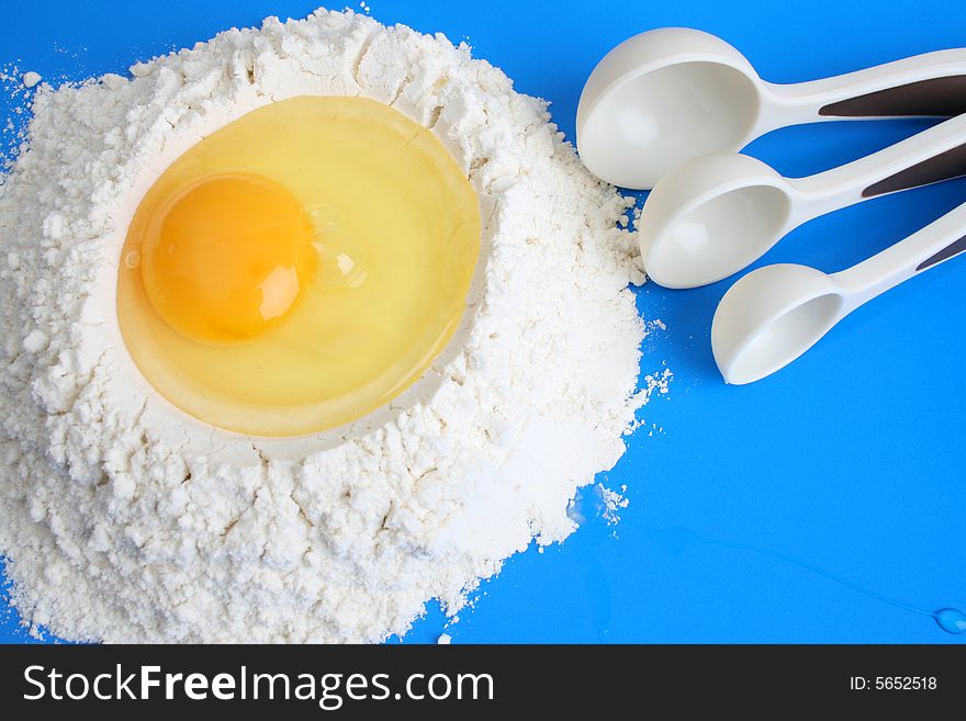 Raw egg in flower with measuring spoons, against a blue background. Raw egg in flower with measuring spoons, against a blue background