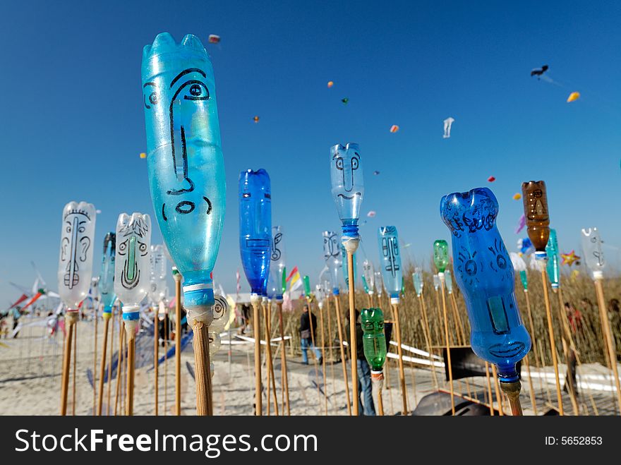 Painted bottles with smiling faces on a beach with deep blue sky and kites in the background