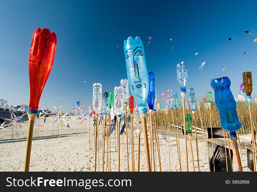 Painted bottles with smiling faces on a beach with deep blue sky and kites in the background