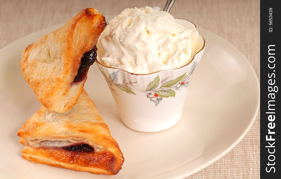 Freshly baked blueberry turnovers resting against a cup of whipped cream. Freshly baked blueberry turnovers resting against a cup of whipped cream