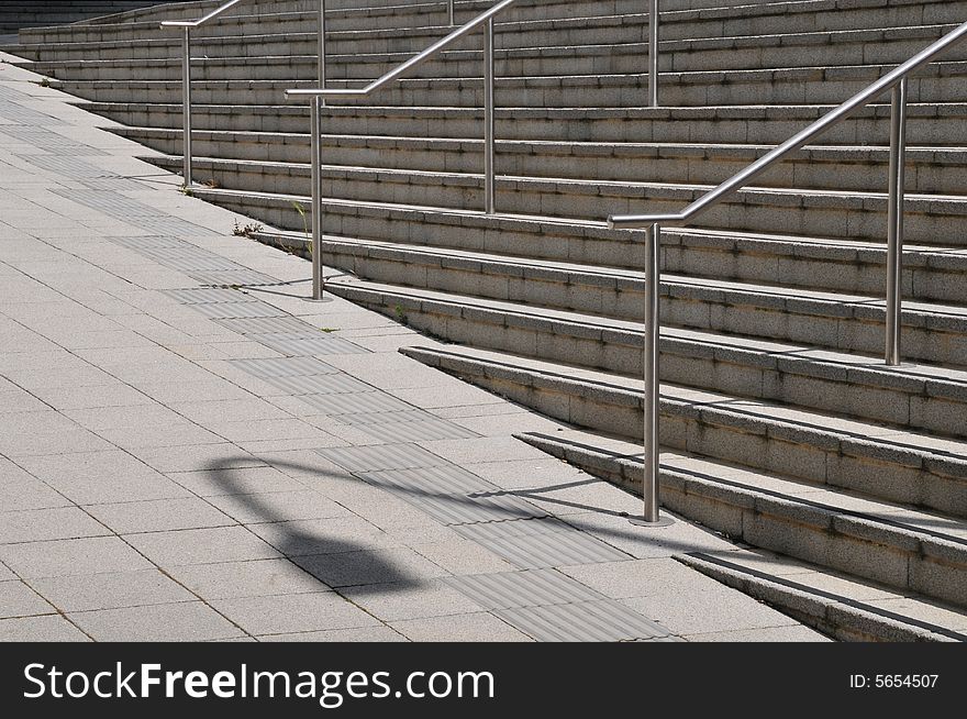 An arrangement of stairs railings and shadows in a pedestrianized urban environment