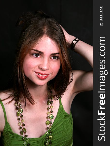 Portrait of a smiling beautiful teenage girl with green beads on her neck is busy styling her hair against black back-ground. Portrait of a smiling beautiful teenage girl with green beads on her neck is busy styling her hair against black back-ground.
