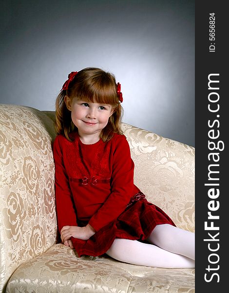 Cute preschool aged girl in red dress on couch looking up and away as if she is hiding something. Cute preschool aged girl in red dress on couch looking up and away as if she is hiding something