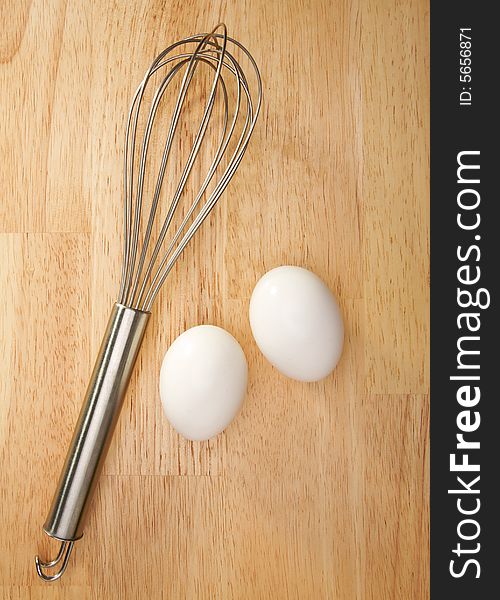 Whisk and Eggs on a wooden background.